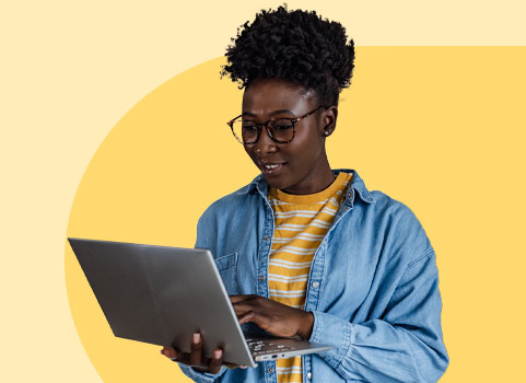 Woman wearing glasses standing in front of orange and pink background, looking at laptop she is holding.