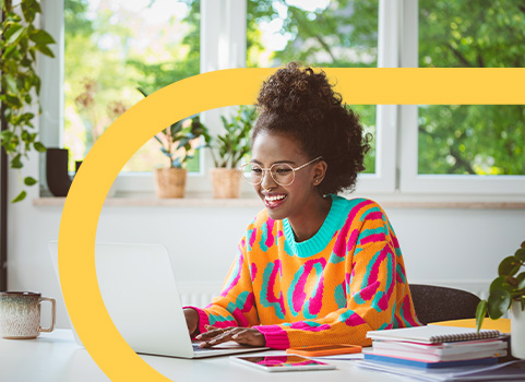 Girl in bright sweater studying with pile of books and laptop.