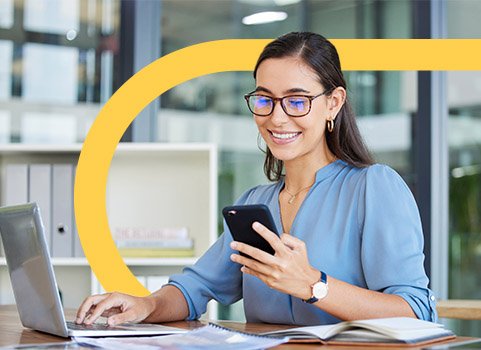 Woman in glasses using phone and laptop for work.