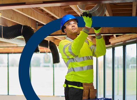 Man in yellow safety gear and blue hard hat installing duct.