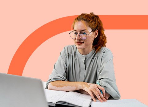 woman with red hair and glasses writing notes from a laptop.