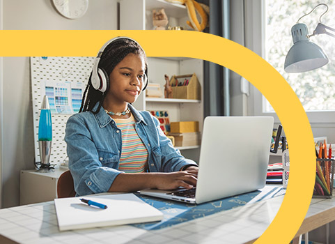 Girl wearing denim jacket in headphones using laptop.