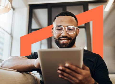 Man wearing glasses sitting on couch and scrolling on tablet.