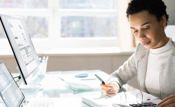 A person with dark skin and dark hair wears a suit and uses a calculator