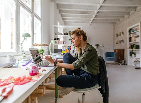 A person sits on a chair in a creative studio, light filled studio, working on a computer